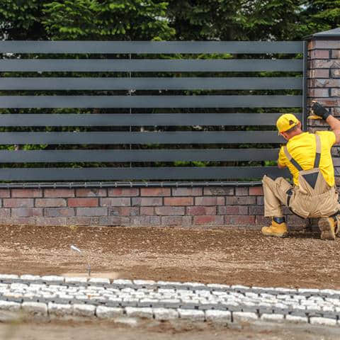 A horizontal-slat fence panel being installed between masonry posts