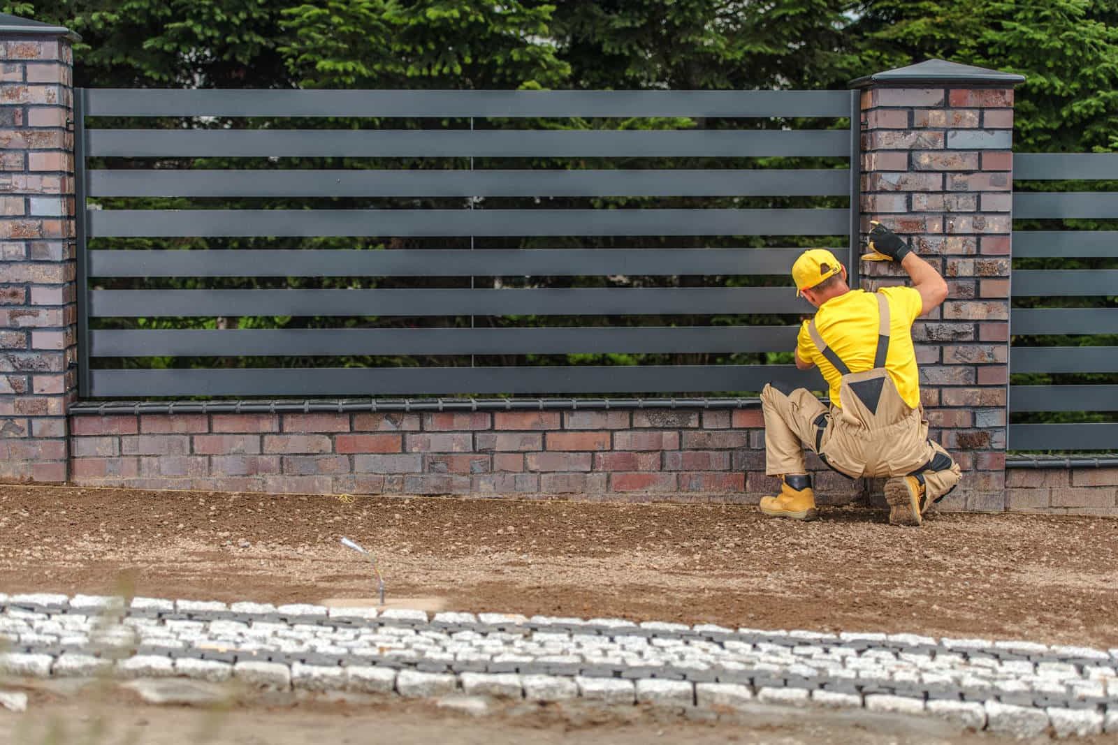 A horizontal-slat fence panel being installed between masonry posts